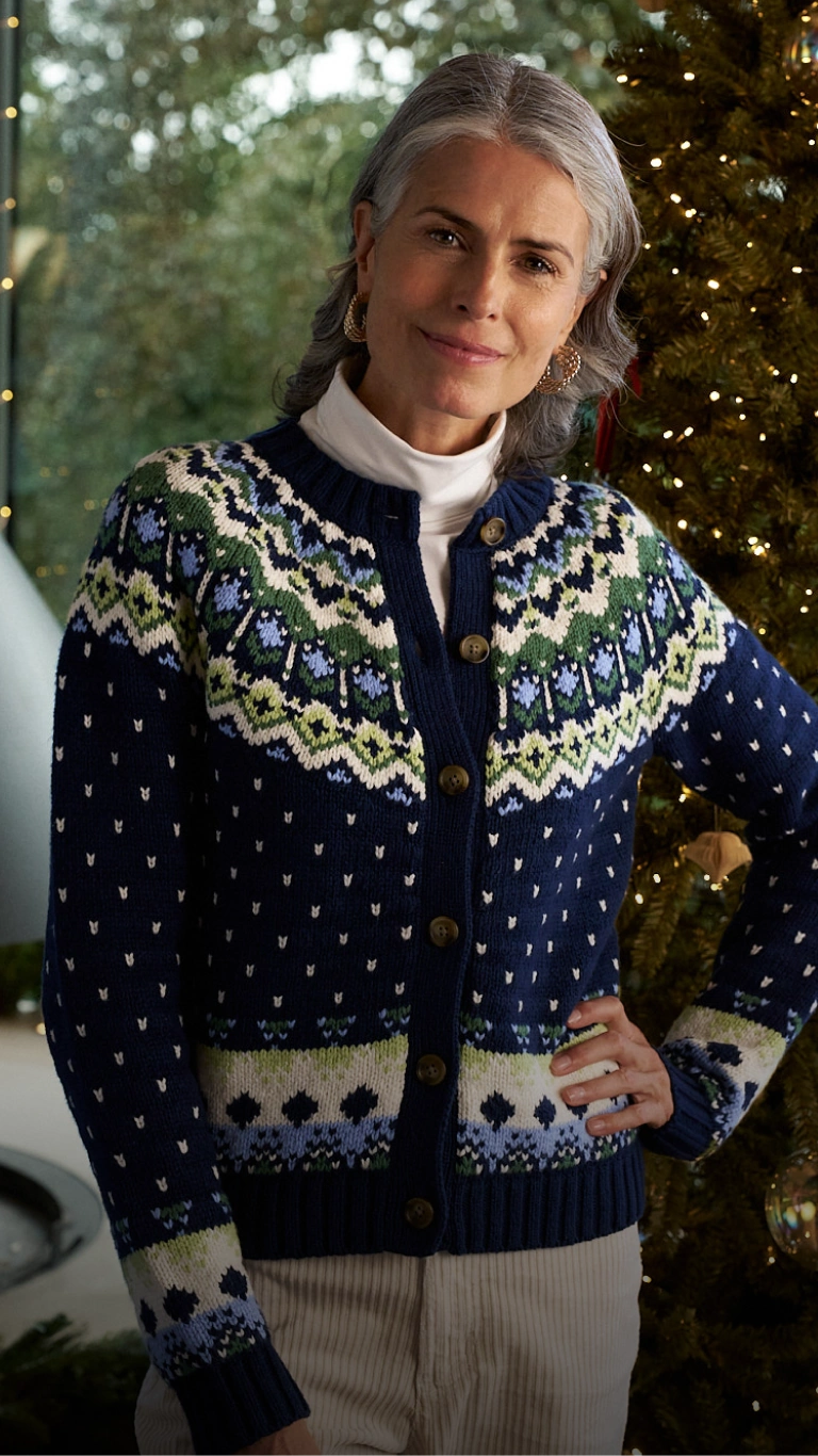 Frau trägt eine marineblaue Strickjacke mit Fair-Isle-Muster vor einem geschmückten Weihnachtsbaum