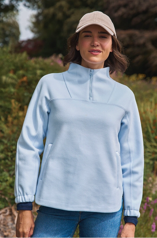 Frau trägt einen hellblauen Pullover mit Reißverschluss und eine Kappe im Freien