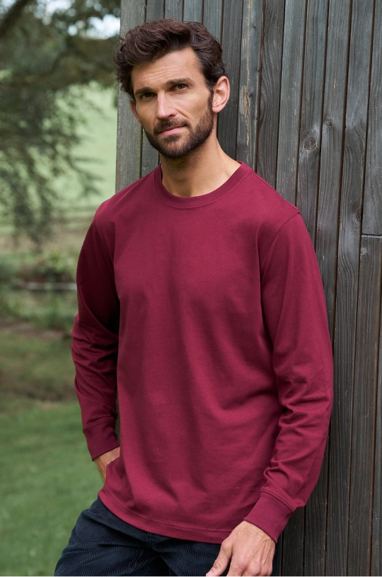 Mann trägt ein bordeauxrotes Sweatshirt mit Rundhalsausschnitt und eine dunkle Jeans im Freien